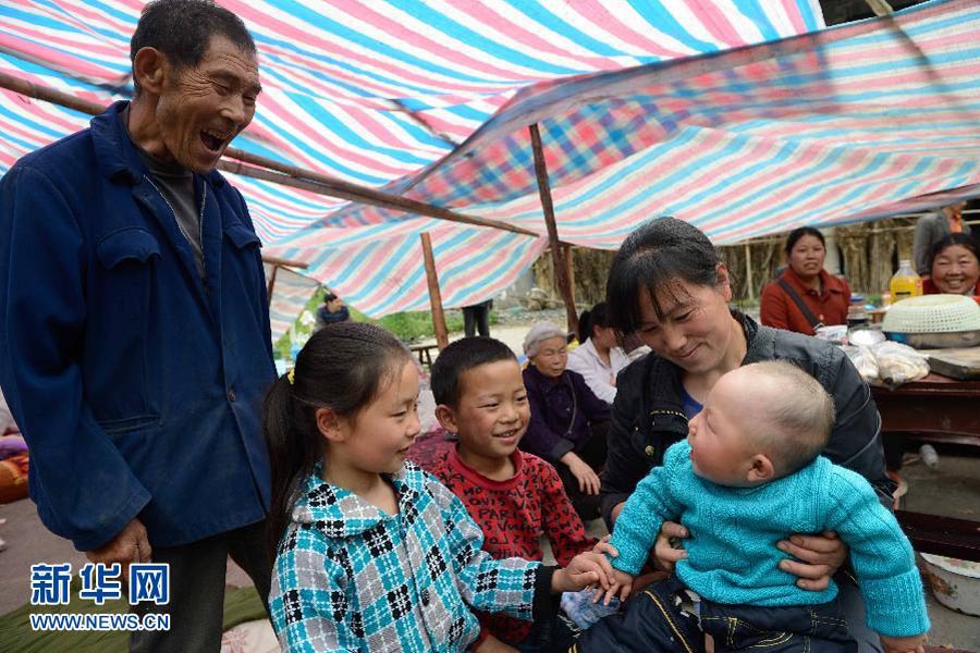 　4月21日，太平鎮春光村溪口上組，張大爺（左）在逗不到8個月大的孫子。目前，“4·20”地震蘆山縣太平鎮仍然余震不斷。但在災區的鄉村，在臨時扎起的帳篷裡，隨時可見孩子們天真的笑臉。突如其來的災難給他們的家園留下了印記，但沒能阻擋笑容在他們臉上綻放。有孩子，有笑容，就有希望。 新華社記者 李橋橋攝