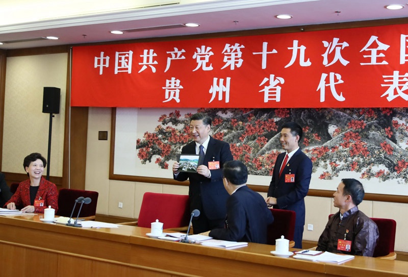 10月19日，習近平同志參加黨的十九大貴州省代表團討論。這是遵義市播州區花茂村黨總支書記潘克剛將一幅鳥瞰村子新貌的照片送到習近平面前。習近平起身接過照片，邊看邊稱贊：“這是風景畫，很漂亮！”新華社記者 蘭紅光 攝